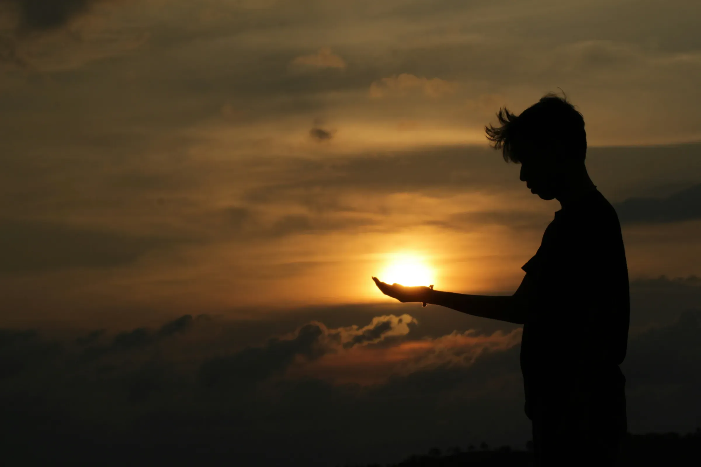 La sagoma di un ragazzo al tramonto con il sole nel palmo della mano